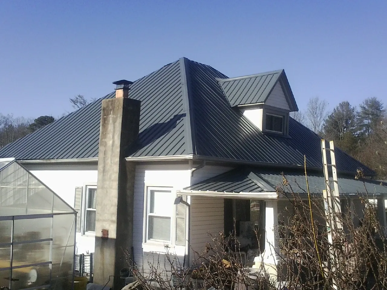 Dark blue standing seam metal roof on a white farmhouse with dormer — Slate & Tile Roof Repair by Roofing Brothers in South Gardiner
