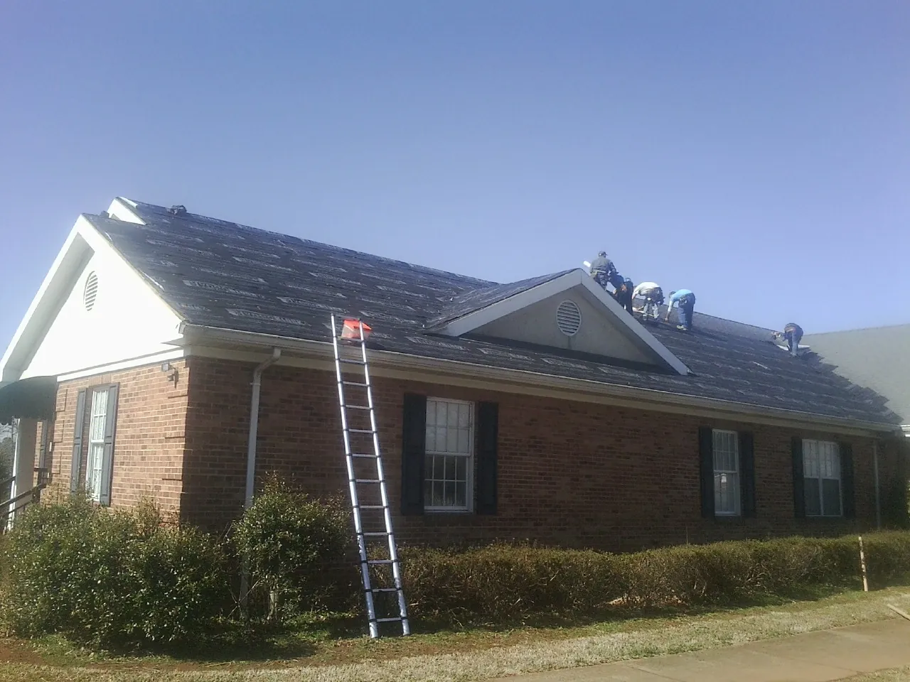 Crew tearing shingles off a brick ranch roof with a ladder set — Emergency Roof Repair work by our crew in South Gardiner