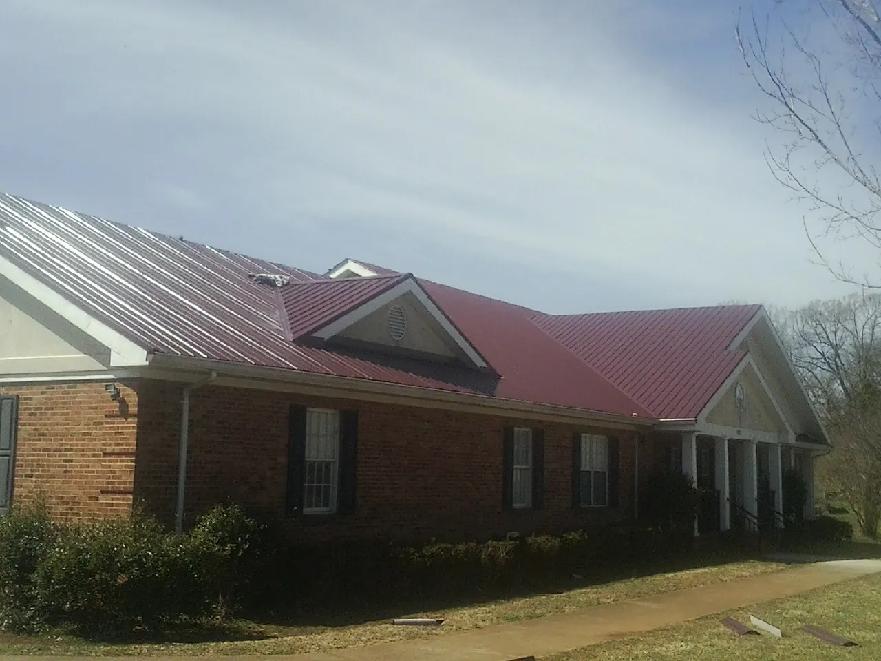 Red metal roof with gabled entries on a long brick building, from a Hail Damage Roof Repair job in South Gardiner