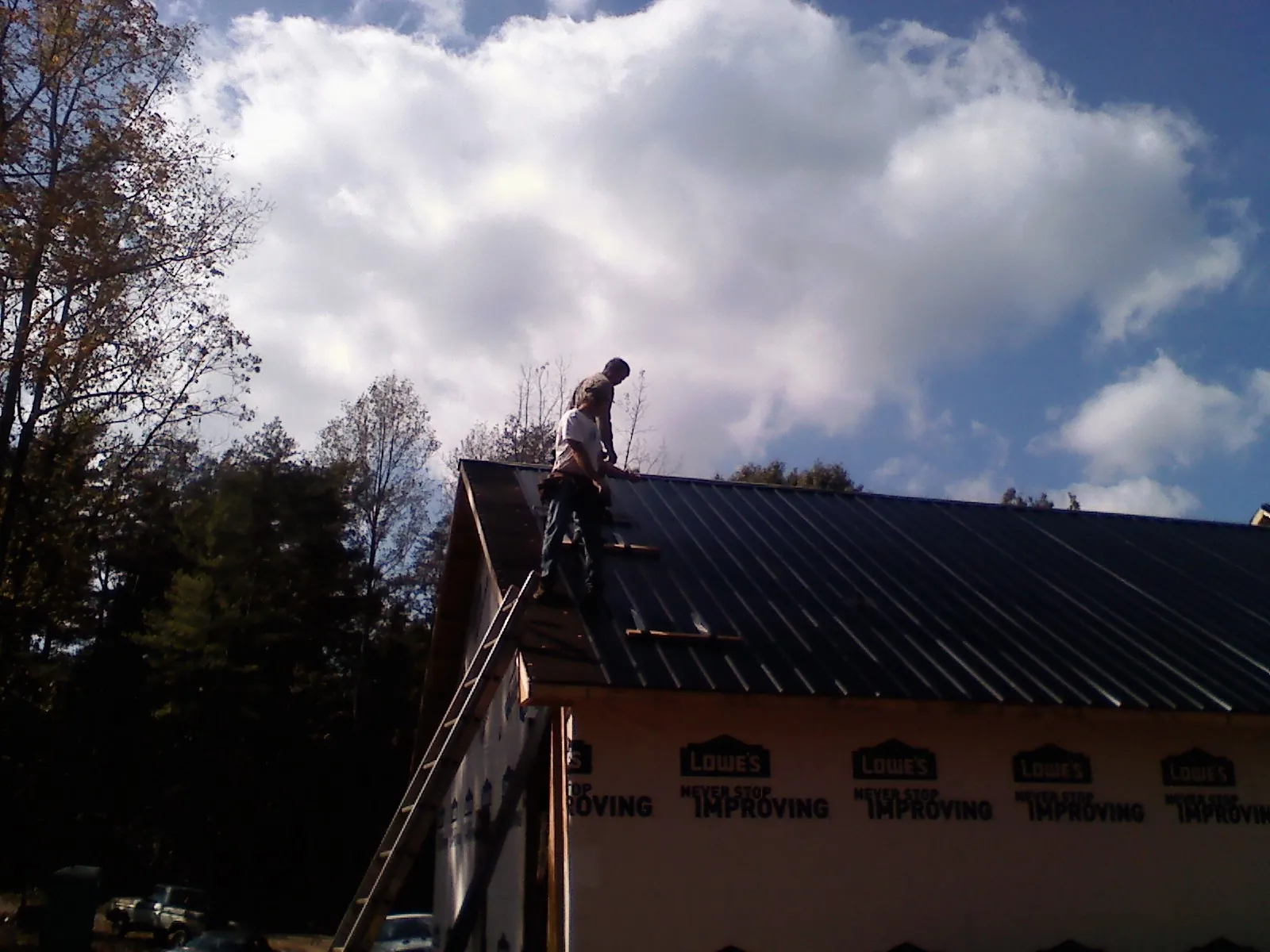Roofer fastening dark metal panels high against a cloudy sky, from a Roof Inspection job in South Gardiner