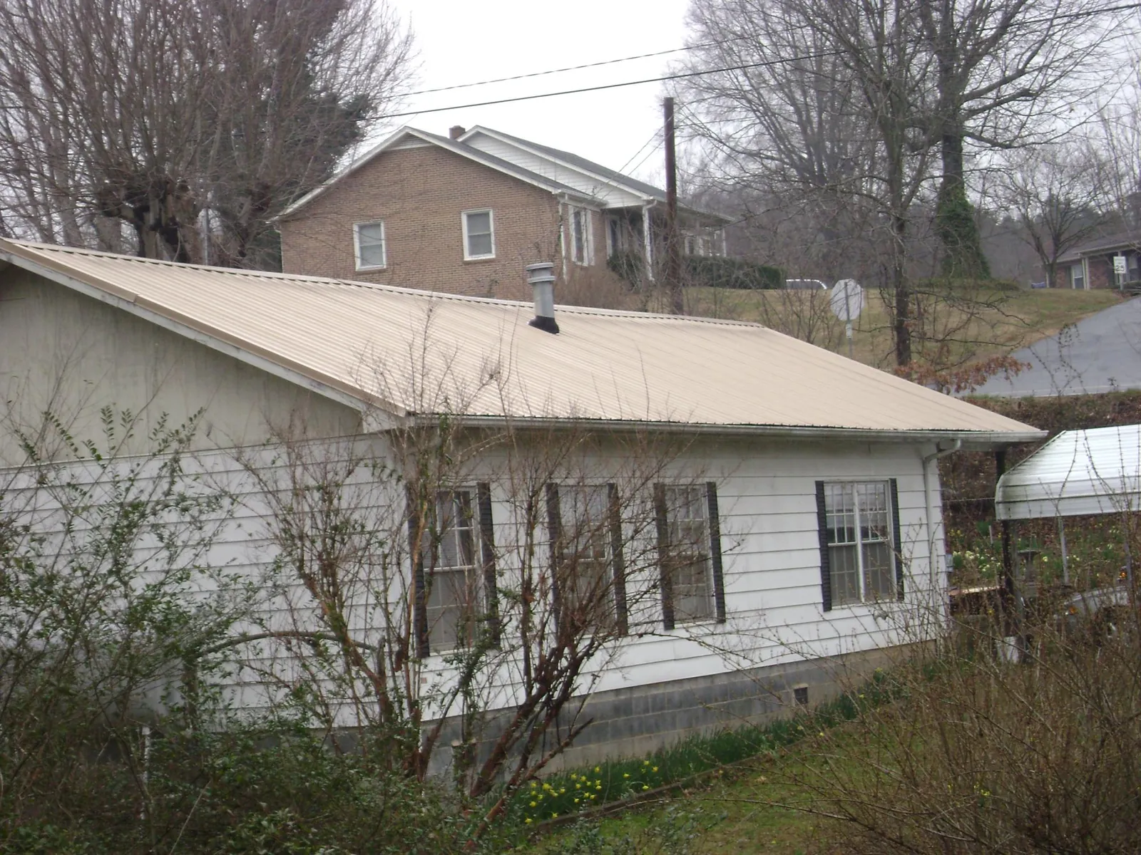 Tan metal roof on a white sided house set into a hillside — Commercial Roofing by Roofing Brothers in South Gardiner