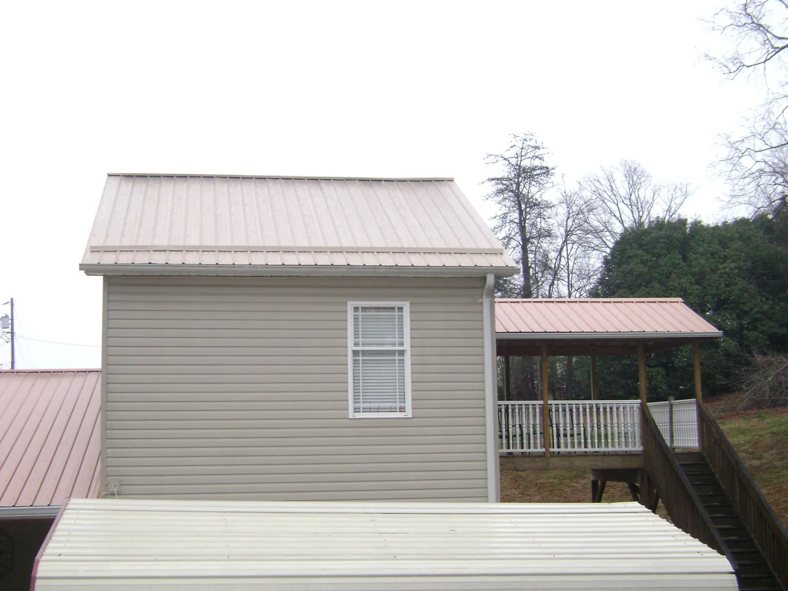 Tan metal roofs on a two story addition and attached porch, from a Roof Replacement job in South Gardiner